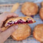 a hand holding a cherry hand pie with a bite in it