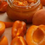 a jar of homemade apricot jam with slices of apricots and habaneros surrounding it